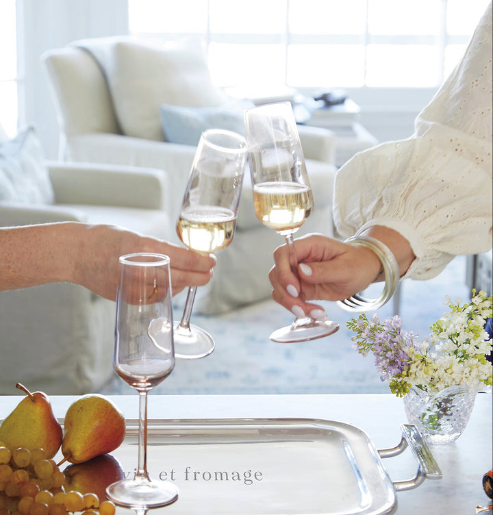 Two people clinking champagne glasses with a tray of fruit and cheese on a marble surface.
